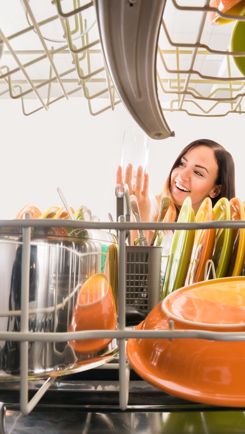 A young woman is taking a clean glass out of a dish washer.